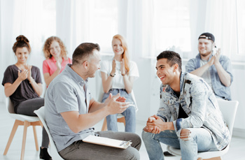Two men sitting down together laughing whilst other people are watching them