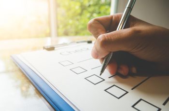 A checklist on a clipboard with someone about to mark a box