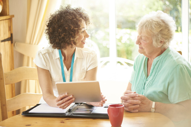 A lady holding an electronic tablet whilst talking to an elderly woman