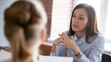 Lady with brown hair and blue shirt talking to colleague