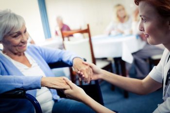 care worker and elderly female resident joining hands and smiling
