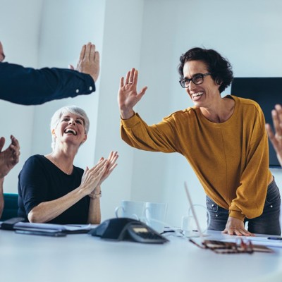  Five colleagues celebrating around a meeting table with high-fives and clapping in a modern office