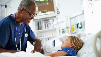 A consultant speaks with a young child on an NHS hospital ward.