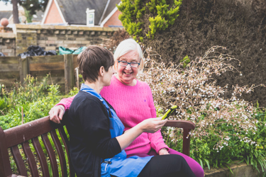 A nurse and an elderly woman sitting outside together on a bench