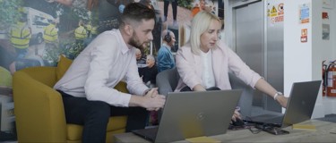 A man and woman sharing their laptop screens with each other.