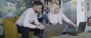 A man and woman sharing their laptop screens with each other.