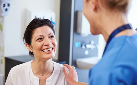A lady smiling whilst a nurse has a hands on her shoulder 