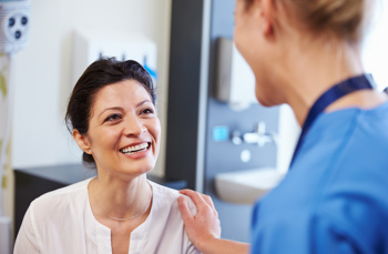 A lady smiling whilst a nurse has a hands on her shoulder 