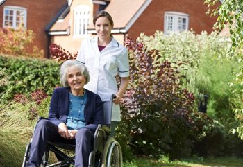 A care worker and an elderly lady in a wheelchair in front of a care home
