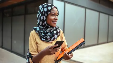 A woman wearing a patterned headscarf holding a mobile phone and documents representing a lawyer engaging with legal software workflows