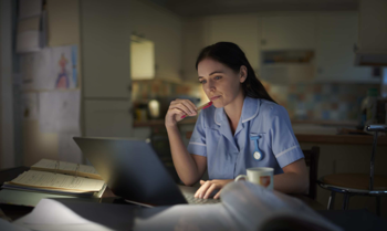 A care worker sitting at a desk in a care home, in front of a laptop, holding a pen in her hand.