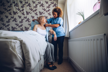A carer helping an elderly lady out of bed.