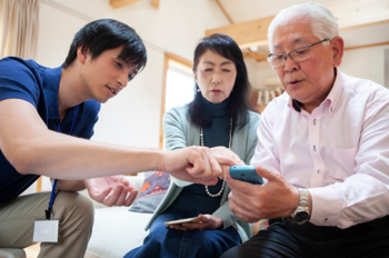 male care worker showing an elderly couple how to use an electronic device