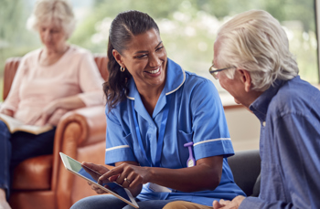 A black woman who is a nurse laughing with a white elderly man