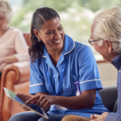 A black woman who is a nurse laughing with a white elderly man