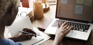 Professional working on a laptop while taking notes during onboarding process