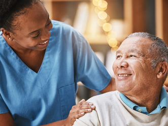Care worker gently touching the shoulder of an elderly male resident. They are both smiling.