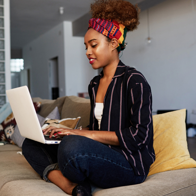 Woman sat on sofa cross legged with laptop on lap