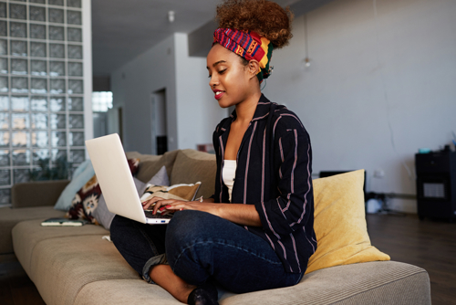 Woman sat on sofa cross legged with laptop on lap