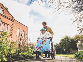 carer pushing a client's wheelchair through a garden