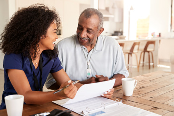 care worker and elderly man sitting together at a table, having a discussion and looking at documents