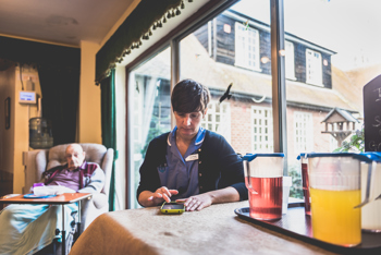 A carer on her phone at a table with a care recipient sat behind her.
