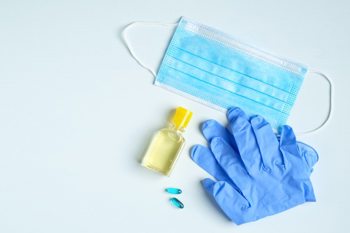 a pair of surgical gloves, a surgical mask and a yellow bottle of disinfectant on a blue surface