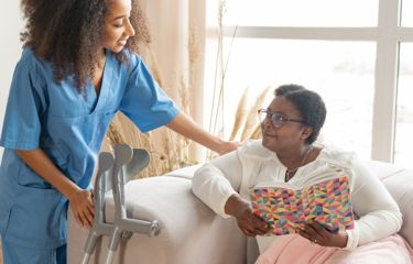 A black nurse assisting an older black woman