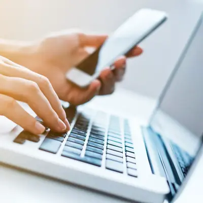 Person using laptop and mobile device to manage client onboarding and communication