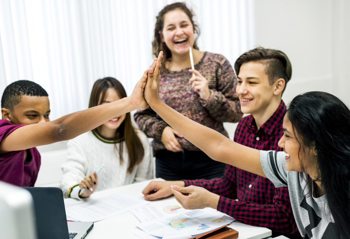 a group of people sitting around a table, smiling and high-fiving each other