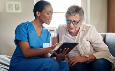 A black nurse showing something to an elderly lady on the tablet 