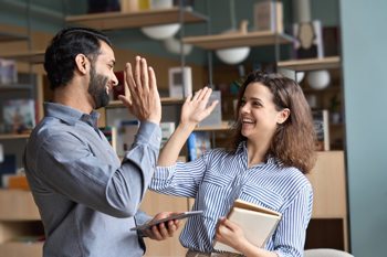 two young people holding notebooks high-fiving each other