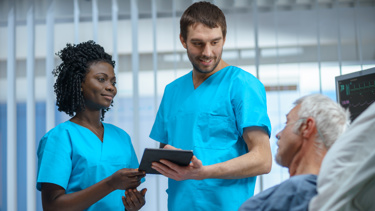 A black woman and a white male consulting a unwell elderly man who is laying in a hospital bed