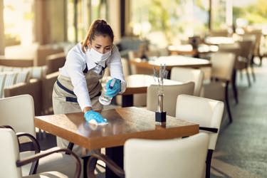 Female waitress wearing face mask cleaning tables