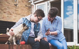 A woman showing a care planner app on her phone to a boy who is stroking his dog 