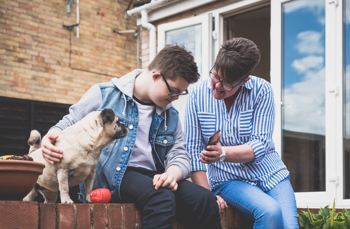 A woman showing a care planner app on her phone to a boy who is stroking his dog 