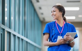 A nurse walking and smiling with a tablet in her hand