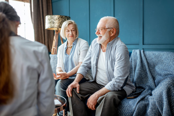 A care worker sitting together with an elderly couple and having a conversation.
