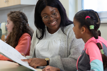 two young girls in a classroom with female teacher
