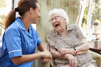 care worker and elderly resident sitting together in the sunroom, sharing a laugh