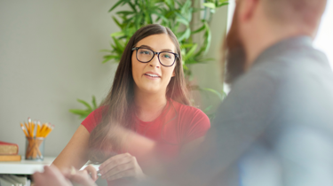 Lady in glasses and pink t-shirt speaking to colleague