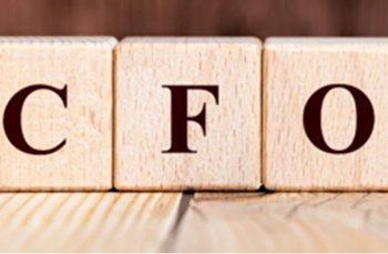 Wooden blocks spelling “CFO” on a wooden surface with a wood-panelled background