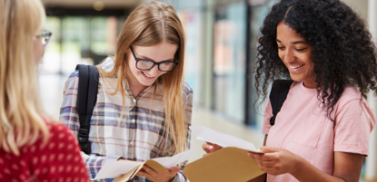 Three female school students opening assessment results in school corridor