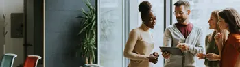 Human + AI partnership concept - a group of four people talking by the window in an office envirnment