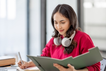 image of a dark-haired woman looking at a dossier and writing ideas down