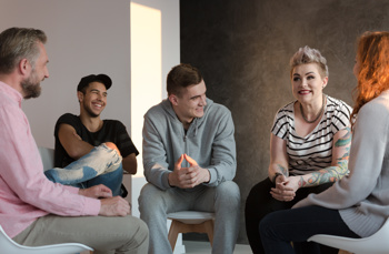 A group of young people sitting down together discussing and smiling between each other