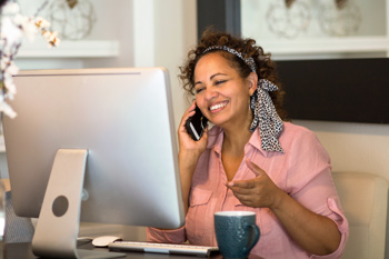 Care worker sitting at a desk in front of a computer screen, talking on the phone.