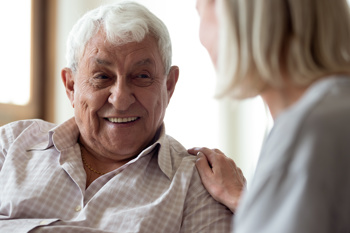 An elderly man smiling at a lady with her hand on his shoulder.