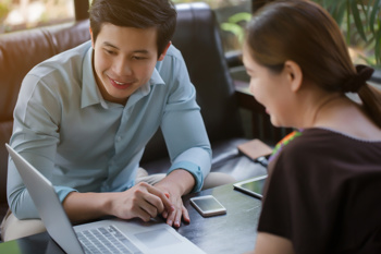 Two colleagues huddled around a laptop smiling