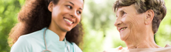 A young female carer smiling at an elderly female who is smiling back at her